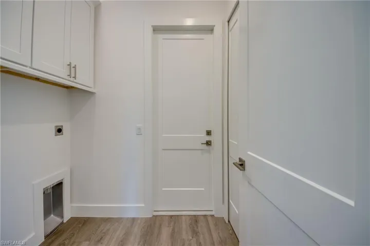 Laundry room featuring light wood-type flooring, electric dryer hookup, and cabinet space