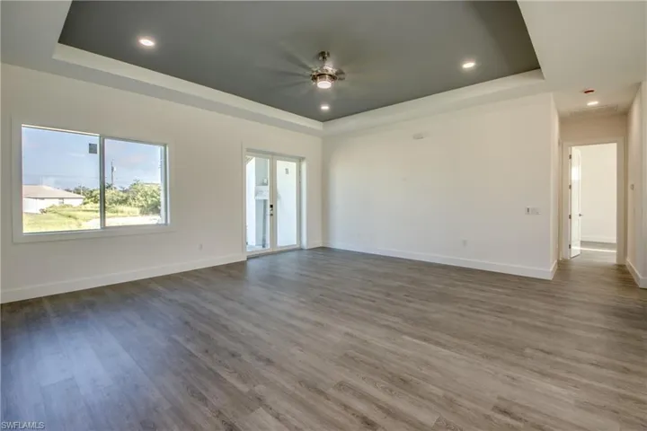 Unfurnished room featuring a raised ceiling, wood finished floors, recessed lighting, ceiling fan, and french doors