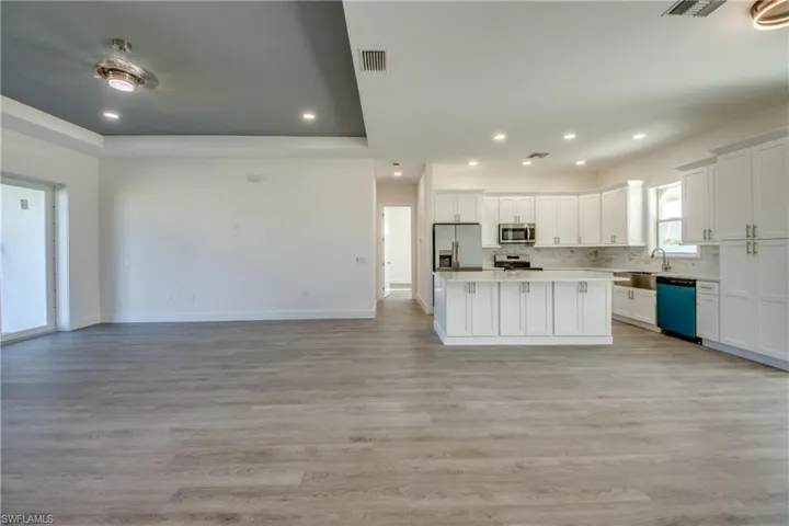 Kitchen with open floor plan, a center island, white cabinets, stainless steel appliances, and light wood-style flooring