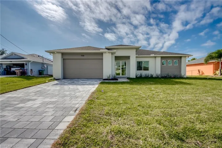 Coastal modern house featuring a front lawn, decorative driveway, stucco siding, and an attached garage