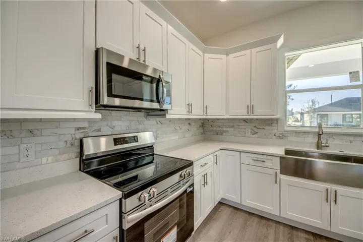 Kitchen with stainless steel appliances, white cabinetry, backsplash, light stone counters, and light wood finished floors