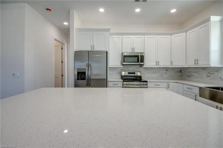 Kitchen with appliances with stainless steel finishes, recessed lighting, white cabinetry, tasteful backsplash, and light stone counters