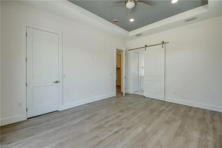 Unfurnished bedroom featuring a barn door, light wood-style flooring, a tray ceiling, ceiling fan, and recessed lighting