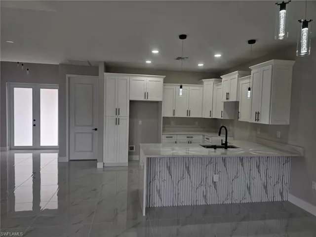 Kitchen featuring light stone countertops, sink, decorative light fixtures, french doors, and white cabinets