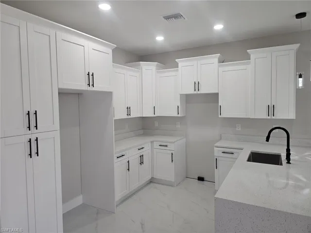 Kitchen featuring light stone countertops, sink, white cabinetry, and hanging light fixtures