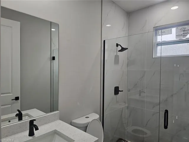 Bathroom with toilet, a shower with door, and vanity