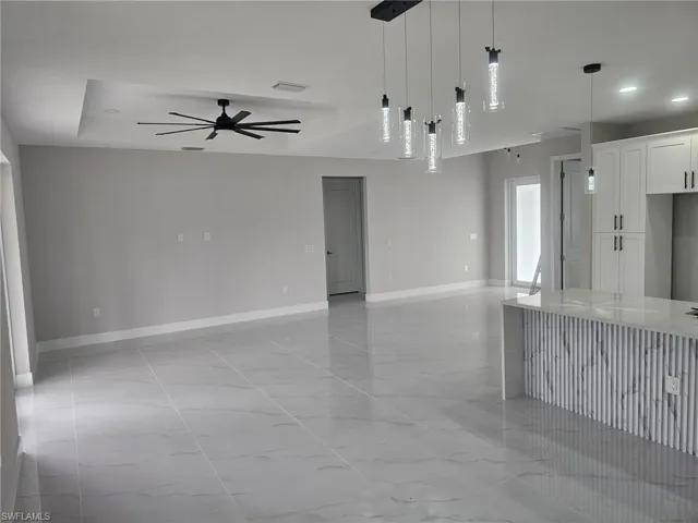 Kitchen featuring ceiling fan, hanging light fixtures, white cabinetry, light stone countertops, and a tray ceiling