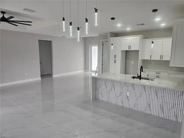 Kitchen featuring white cabinetry, ceiling fan, sink, hanging light fixtures, and light stone counters