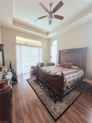 Bedroom featuring a raised ceiling, access to exterior, wood finished floors, and ceiling fan