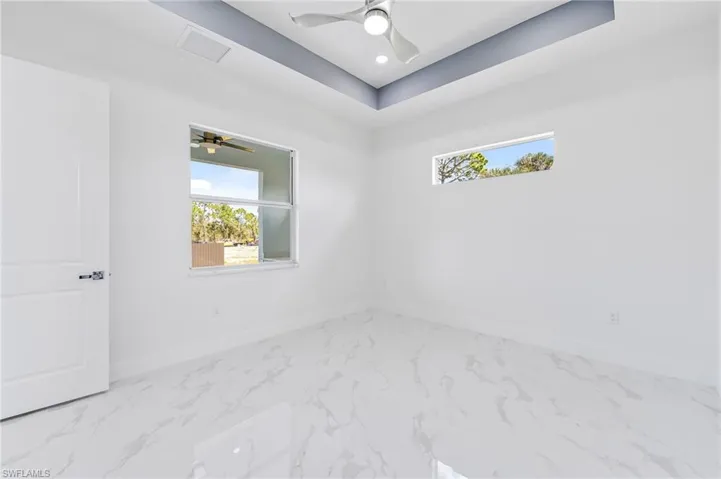 Tiled empty room featuring ceiling fan and a raised ceiling