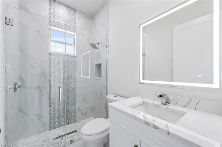 Bathroom with a shower with door, toilet, and vanity with extensive cabinet space