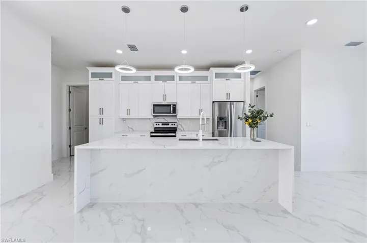 Kitchen with hanging light fixtures, light tile floors, a kitchen island with sink, and appliances with stainless steel finishes
