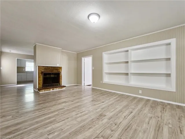 Unfurnished living room featuring a brick fireplace, built in features, and hardwood / wood-style flooring
