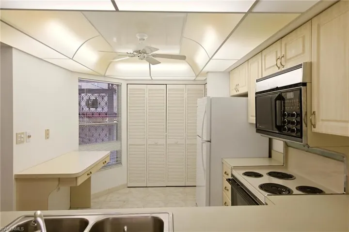 Kitchen with white appliances, light countertops, a ceiling fan, a peninsula, and light tile patterned floors