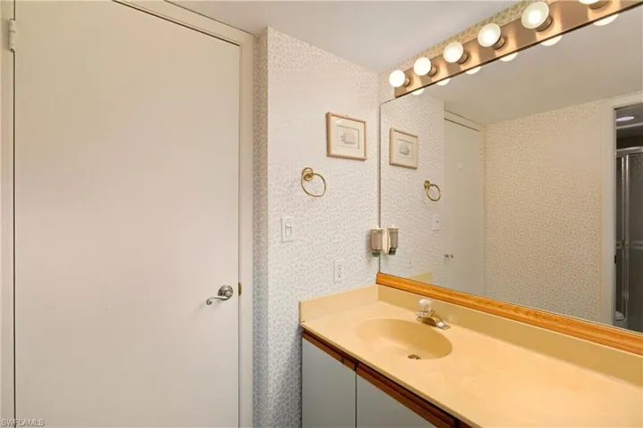 Bathroom with wallpapered walls, vanity, and an enclosed shower