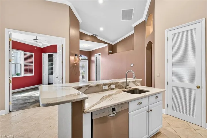 Kitchen featuring vaulted ceiling, light stone counters, light tile patterned floors, ornamental molding, and stainless steel dishwasher