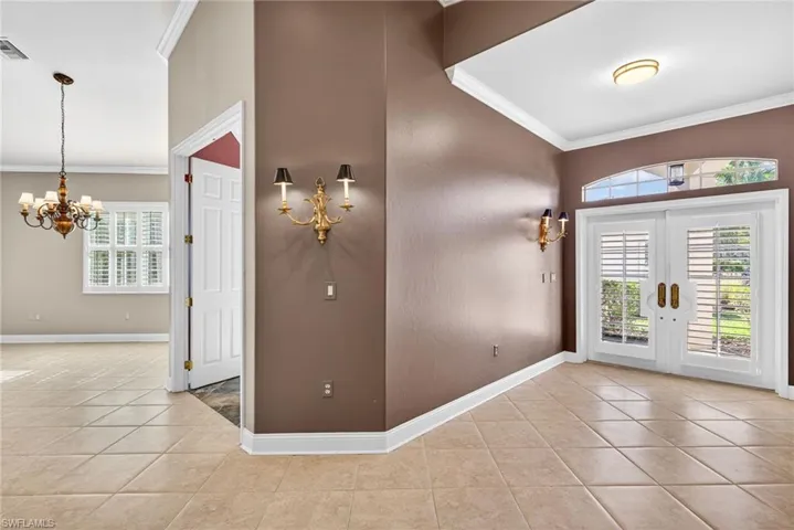 Entryway with crown molding, hanging lights, light tile patterned floors, and french doors