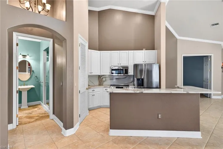 Kitchen with white cabinets, stainless steel appliances, a high ceiling, light stone counters, and a kitchen island