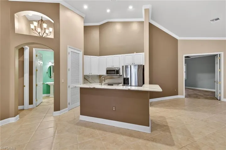 Kitchen featuring arched walkways, white cabinets, crown molding, stainless steel appliances, and a chandelier