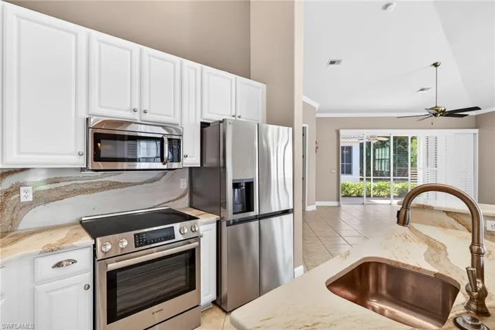 Kitchen featuring stainless steel appliances, light stone countertops, ornamental molding, white cabinetry, and a ceiling fan