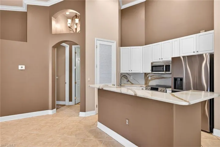 Kitchen with white cabinets, light stone counters, stainless steel appliances, ornamental molding, and arched walkways