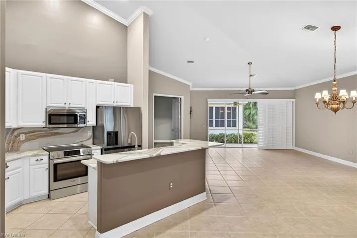 Kitchen with vaulted ceiling, ornamental molding, stainless steel appliances, light stone countertops, and a ceiling fan