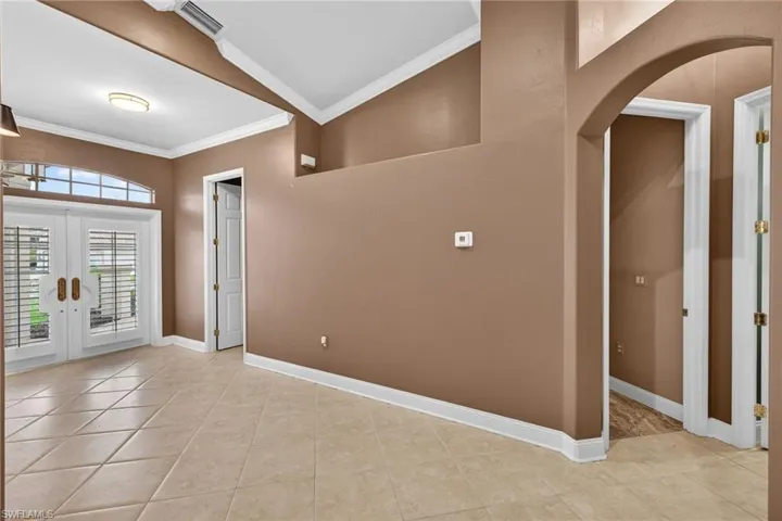 Foyer entrance with crown molding, arched walkways, french doors, and light tile patterned flooring