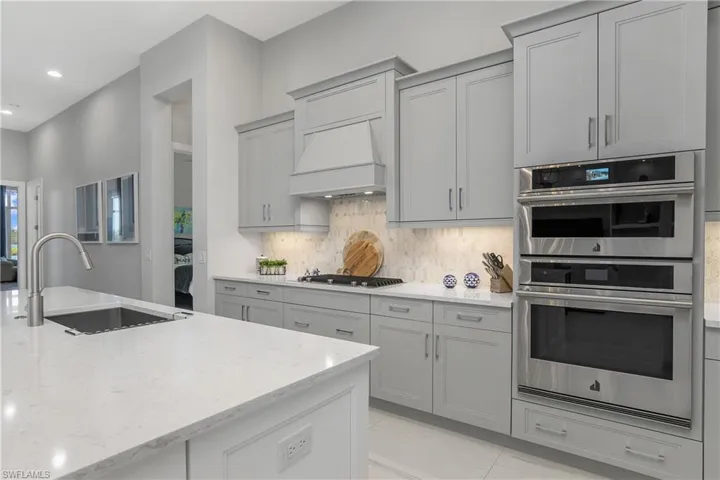 Kitchen with sink, light stone counters, gray cabinets, decorative backsplash, and appliances with stainless steel finishes