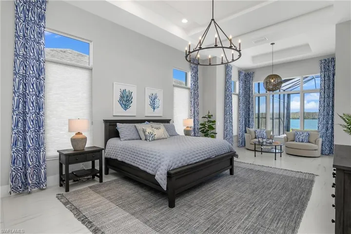 Bedroom featuring a water view, an inviting chandelier, multiple windows, and a tray ceiling