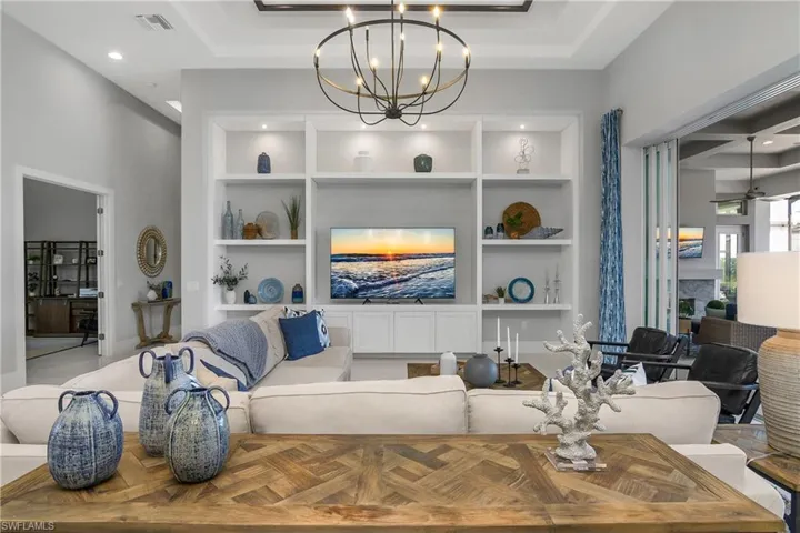 Living room with an inviting chandelier, built in features, and coffered ceiling with custom woodwork.