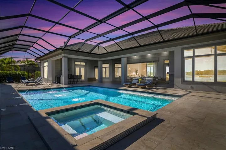 Pool at dusk featuring pool water feature, glass enclosure, a patio area, and an in ground hot tub