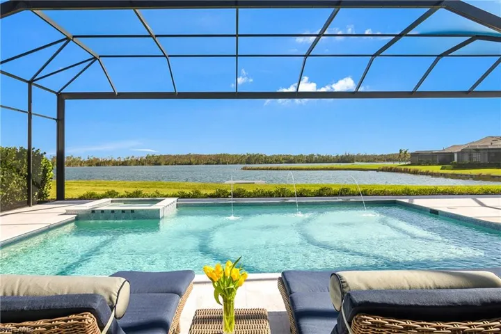 View of pool with an in ground hot tub, pool water feature, a water view, and glass enclosure
