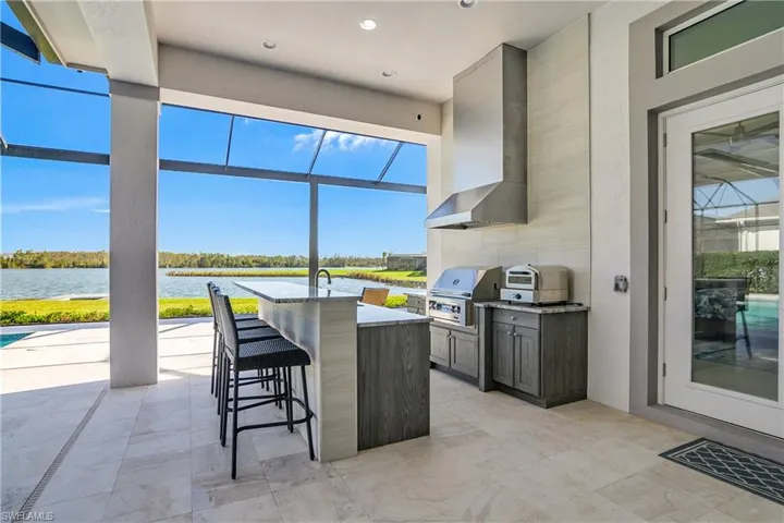 View of patio with a lanai, a wet bar, exterior kitchen, a water view, and a grill
