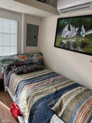 Bedroom with a wall mounted air conditioner, wood finished floors, and electric panel