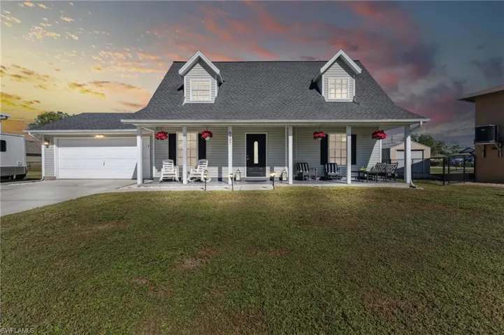 View of front of home with central air condition unit, a yard, covered porch, and a garage