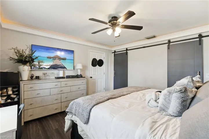 Bedroom with a barn door, dark hardwood / wood-style floors, and ceiling fan