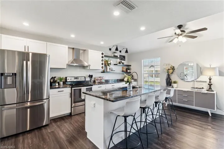 Kitchen featuring white cabinets, wall chimney range hood, a kitchen island with sink, and appliances with stainless steel finishes