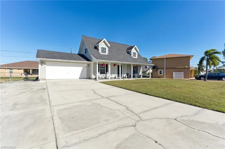 Cape cod home with covered porch, a garage, and a front lawn