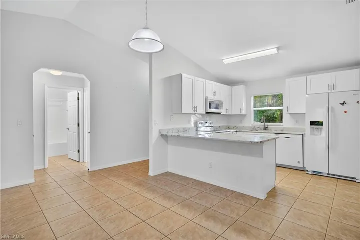 Kitchen featuring lofted ceiling, white appliances, light tile patterned floors, white cabinets, and pendant lighting