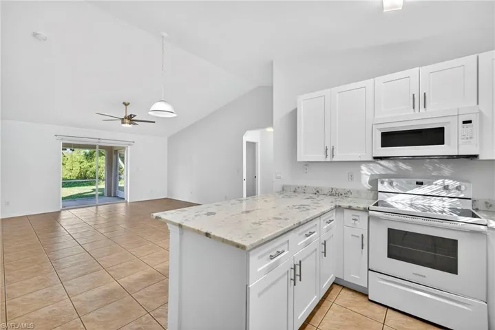 Kitchen with white appliances, light tile patterned flooring, white cabinets, lofted ceiling, and ceiling fan
