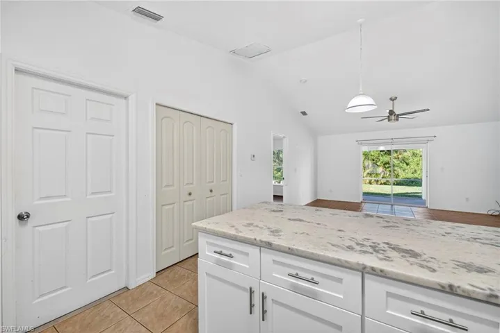 Kitchen featuring white cabinetry, light tile patterned flooring, light stone counters, decorative light fixtures, and ceiling fan