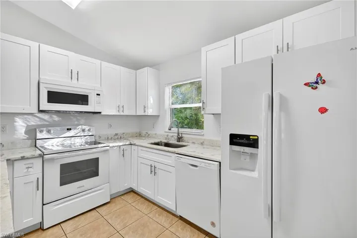 Kitchen with white appliances, white cabinets, light stone counters, and lofted ceiling
