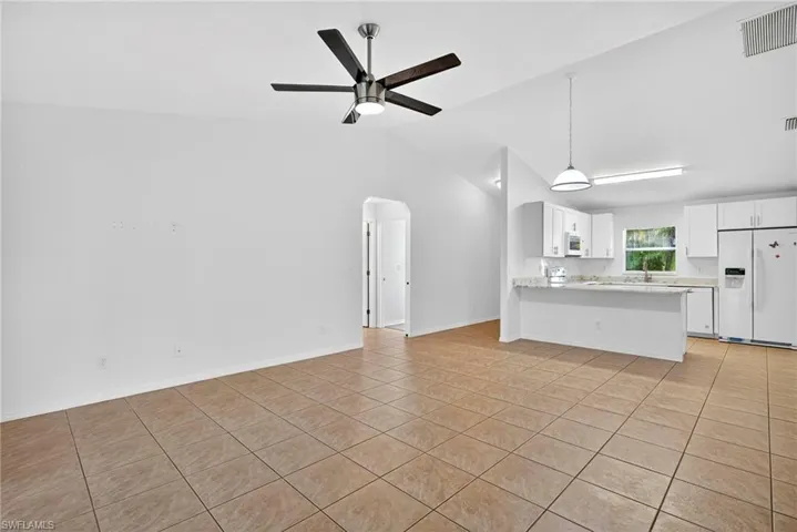 Unfurnished living room featuring arched walkways, vaulted ceiling, light tile patterned floors, and a ceiling fan
