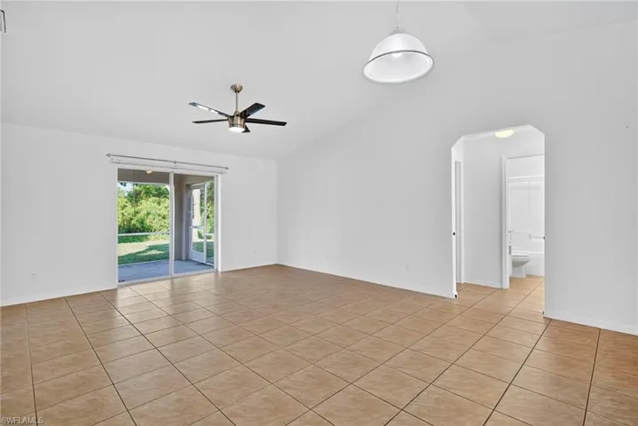 Unfurnished room with vaulted ceiling, light tile patterned flooring, arched walkways, and ceiling fan