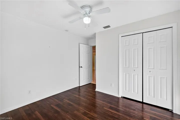 Unfurnished bedroom with dark wood-type flooring, a closet, and a ceiling fan