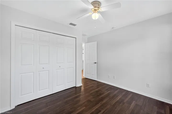 Unfurnished bedroom featuring dark wood-style flooring, a closet, and a ceiling fan