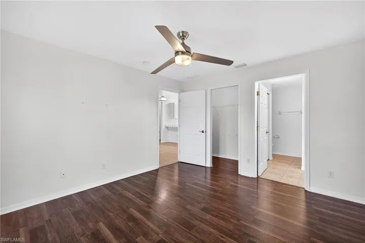 Unfurnished bedroom with dark wood-style flooring, a ceiling fan, a spacious closet, and ensuite bathroom