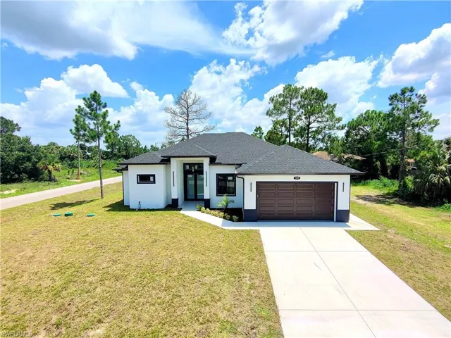 View of front of home featuring a garage, concrete driveway, a front lawn, a shingled roof, and stucco siding