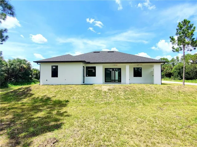 Rear view of house with ceiling fan, a yard, and stucco siding