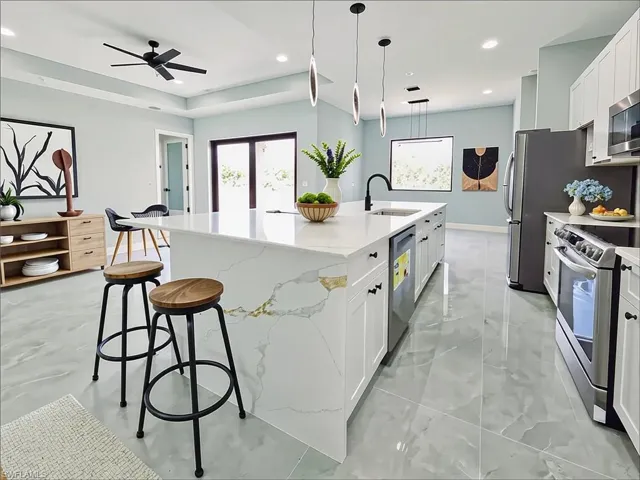 Kitchen featuring a center island with sink, a ceiling fan, white cabinets, light stone countertops, and hanging light fixtures
